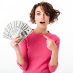 Portrait of an excited pretty girl pointing finger at bunch of money banknotes isolated over white background