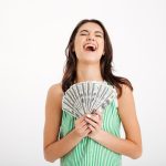 Portrait of a satisfied girl in dress holding bunch of money banknotes and laughing isolated over white background