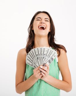 Portrait of a satisfied girl in dress holding bunch of money banknotes and laughing isolated over white background