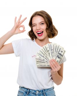 Portrait of a smiling happy girl holding bunch of money banknotes while showing ok gesture and looking at camera isolated over white background