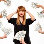 Portrait of young successful businesswoman among money, hands on head over white background.