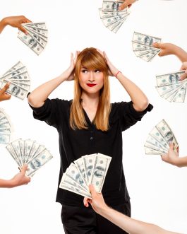 Portrait of young successful businesswoman among money, hands on head over white background.